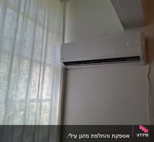 מזגן מותקן על קיר ליד חלון עם וילון